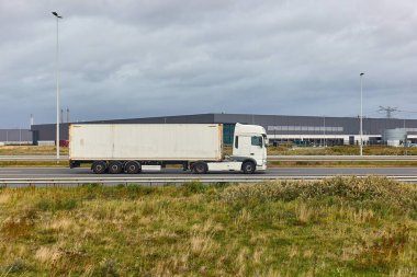 Rotterdam limanında arka planda lojistik deposu olan yarı kamyon yolda.