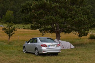 Hohewand, Avusturya - 12 Haziran 2022: Bir ağacın gölgesinde çadır kuran Toyota Corolla 2011 modeli, kamp alanının yanına park etti.