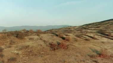 Kuru bitki örtüsü olan insansız hava aracı manzaralı tepeler, uzak kırsal kesimdeki tepenin üzerinde ortaya çıkan köy.