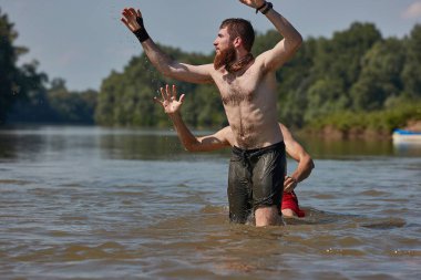 Sahilde suda oynayan bir adam topu yakalayıp suda dövüşmeye çalışıyor.