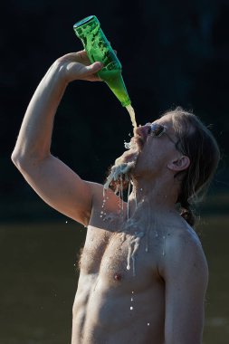 Kumsalda sakallı adam bira içiyor yukarıdan deli gibi bira döküyor.