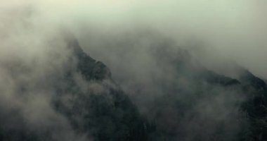 Dağ ormanlarından geçen sis ve bulutlar, sisli manzara, keskin kayalık uçurumlar, dramatik kasvetli hava, 460 fp 'lik sinematik doğa görüntüleri.