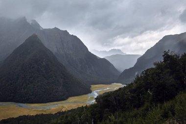 High mountain landscape along the Routeburn Track, Great Walk hiking trail in New Zealand South Island, foggy cloudy weather, clouds passing over a valley clipart