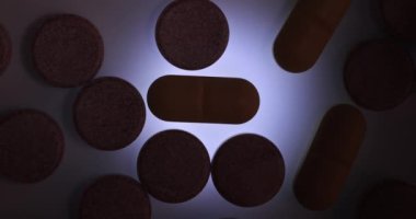 Parlak, şeffaf bir yüzey üzerinde dönen ilaç hapları. Arkası aydınlık, koyu tonu, uyuşturucu porsiyonları...