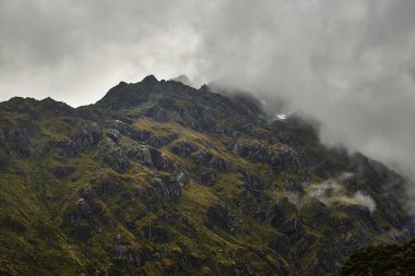 Routeburn Pisti 'ndeki yüksek dağ manzarası Yeni Zelanda Güney Adası' ndaki harika yürüyüş yolu sisli hava, uçurumlar ve göl.