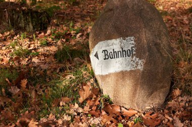 Bahnhof, Alman demiryolu istasyonu, sonbahar ormanlarında bir taşın üzerine yön işareti.