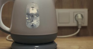 Electric kettle water heater at boiling point for hot beverages, plugged in on the kitchen counter