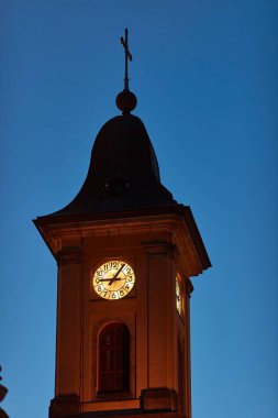 Akşam karanlığında Avrupa 'nın bir şehrinde kilise kulesi, mavi saatte saat aydınlanıyor.