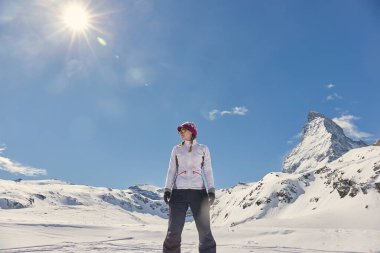 İsviçre 'deki Matterhorn dağının önünde duran bir kadın, mavi gökyüzünde güneş ışığı parlıyor, karlı kış manzarası