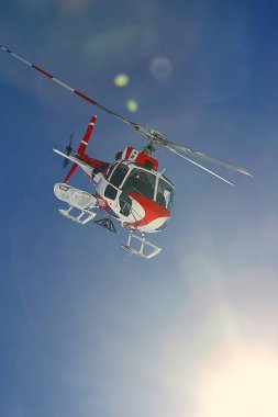 Les 2 Alpes, Fransa - 9 Ocak 2023: kurtarma helikopteri, sisli mavi gökyüzünde güneş ışığı parlaması