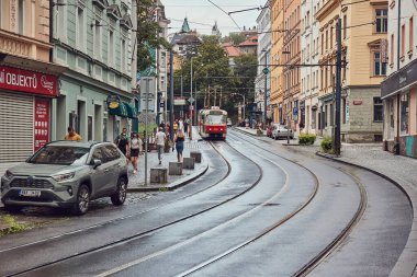 Prag, Çek Cumhuriyeti - 4 Ağustos 2024: Tramvay hattı ve tramvay durağı olan bir caddeyi görmek, yağmurdan sonra ıslak kaldırımlarda yürüyen insanlar. Prag 10. bölge