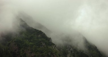 Dağ ormanlarından geçen sis ve bulutlar, sisli manzara, keskin kayalık uçurumlar, dramatik kasvetli hava, sinematik zaman dilimi görüntüleri, hızlı zaman atlaması.