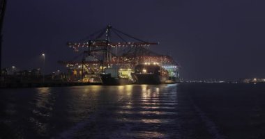 Gece Rotterdam limanındaki kargo konteynırı nakliye terminalinde limanda büyük konteynır gemileri limanda vinçlerle yüklendi.