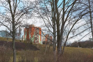 Parkın arkasında ağaçlarla çevrili birçok apartman blokları var.