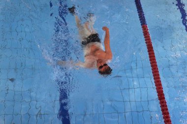 Kapalı yüzme havuzunda yüzen bir adam sırt üstü yüzme alıştırması yapıyor.