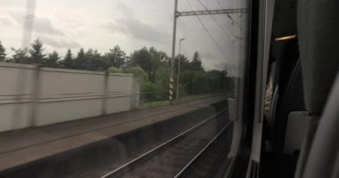 Tren raylarının uzun mesafeli demiryolu yolculuğundaki pencere manzarası, yağmurlu bulutlu hava, ıslak orman manzarası ve istasyon.
