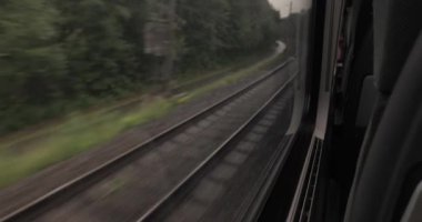 Tren raylarının üzerindeki uzun bir viraj demiryolu yolculuğunun, yağmurlu bulutlu hava, ıslak orman manzarası.