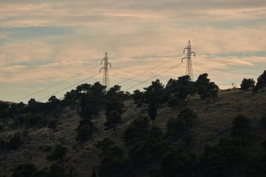 Tepedeki yüksek voltajlı elektrik iletim kolonları.