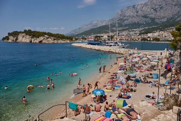 Makarska, Hırvatistan - 29 Temmuz 2024: Pek çok kişi Hırvatistan 'ın Makarska kentinde halka açık bir plajda güneşleniyor ve yüzüyor, sıcak yaz günü dayanılmaz sıcağa sahip