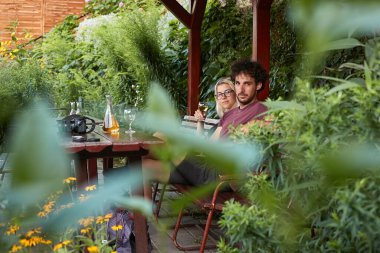 Şarap içen, terasta oturan yeşil bir çalılığın dallarından vurulan bir çift.