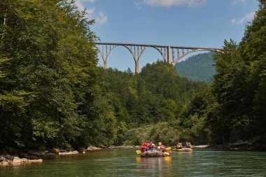 Şişme teknelerle Tara Nehri 'nde rafting grubu turu. Uzakta tanınmayan insanlar var. Tara köprüsü manzaraya hükmediyor