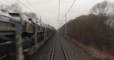 Tren yolculuğu bakış açısı. Yeni araçlar taşıyan bir yük treninin yük vagonlarının yanından geçiyoruz.