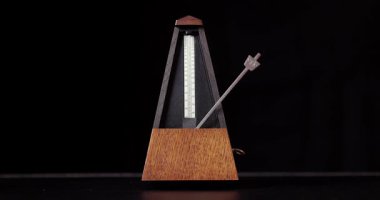 Klasik metronoma tıklayarak bir tablo, siyah arkaplan, yakın plan, yavaş tempo, döngü videosu, düzenli aralıklarla işaretleme