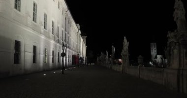 Kutna Hora, Çek Cumhuriyeti 'nin Gotik Katedrali yakınlarındaki aydınlatılmış eski Cizvit Koleji binasının yanında gece yürüyüşü yapıyor. Karanlıkta yürüyen kamera hareketiyle