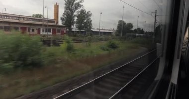 Pardubice, Çek Cumhuriyeti - 4 Ağustos 2024: Demiryolu hattındaki tren penceresi manzarası, yağmurlu bulutlu hava, demiryolu kenarlı sanayi bölgesi