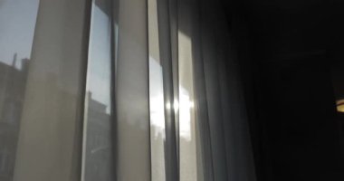 Pencere perdesi dışarıda güneş ışığı var, yorgun insan eli hareket ediyor, perdeyi açıyor, güneşe ve sokağa bakıyor.