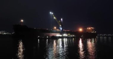 Kargo gemisinin büyük bir yük gemisinden Maasvlakte, Rotterdam limanındaki daha küçük nehir mavnalarına geceleri vinçle yük boşaltma malzemesi.