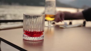 Plaj barında içki içmek, Negroni kokteyli ve masada bir bardak bira..