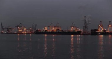 Gece Rotterdam limanındaki kargo konteynırı nakliye terminalinde limanda büyük konteynır gemileri limanda vinçlerle yüklendi.