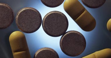 Karanlık, parlak bir yüzey üzerinde dönen ilaç hapları. Arka ışık, koyu ton, ilaç porsiyonları.