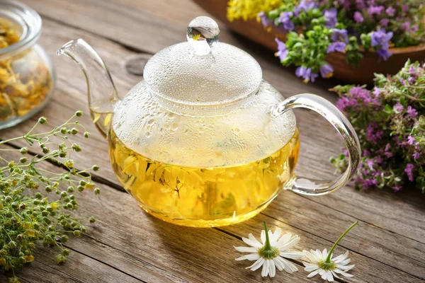 Glass tea kettle of healthy herbal tea, chamomile, calendula, thyme flowers on wooden table. Alternative herbal medicine.