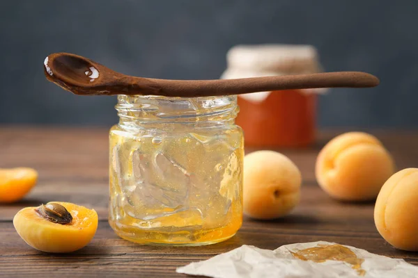 Empty jar of eaten apricot jam. Empty glass jar of homemade apricot jam, spoon and ripe apricot fruits on kitchen table.