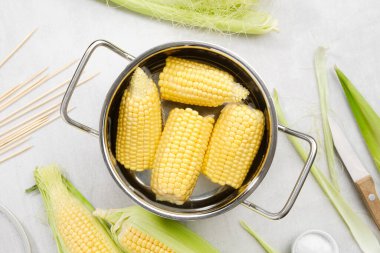 Pişirmeye hazır sarı mısır koçanları, çiğ mısır koçanları, ahşap şişler, mutfak masasında bıçak ve tuz..