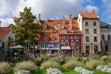 Litvanya 'nın Riga kentindeki Liv Meydanı manzarasında renkli tarihi binalar, yemyeşil alanlar ve popüler bir turizm beldesinde açık hava kafeleri yer alıyor..