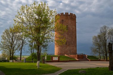 Ortaçağ Kamianet Kulesi, 13. yüzyıldan kalma, yeşil ağaçlar ve bulutlu bir gökyüzü ile çevrili, Kamyenyet, Belarus 'ta bulunan kırmızı tuğlalı bir savunma yapısıdır..