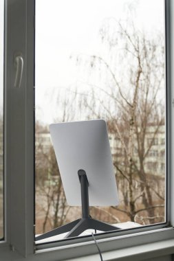 KYIV, UKRAINE - 8 JANUARY 2023: Starlink antenna for receiving signal in window of high rise building.