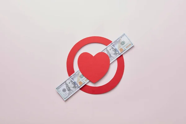 红纸在米色背景的面额钞票的横线上划成圆形 并留有复制空间 爱战胜金钱的创造性概念 被禁止的爱情 — 图库照片