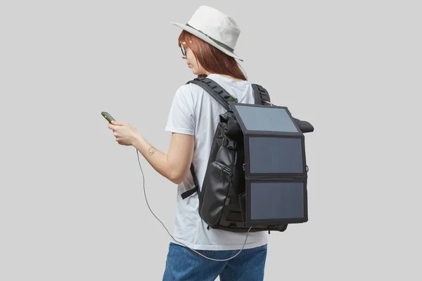 充電ソーラーパネルとバックパックを運ぶ手の中にスマートフォンを持つ少女は ライトグレーの背景に隔離された 持続可能な旅行の概念 — ストック写真