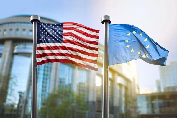 アメリカとヨーロッパの旗は ブリュッセルで欧州議会の建物の背景に対して波を起こします 各国間の協力シンボル ロイヤリティフリーのストック画像