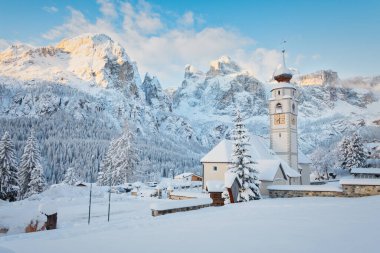 Corvara yakınlarındaki Colfosco (Kolfuschg) kilisesinin arka planında Sella grubu Dolomites dağları, İtalya 'daki Alta Badia kayak merkezindeki taze kar tabakasının altında yer alır..