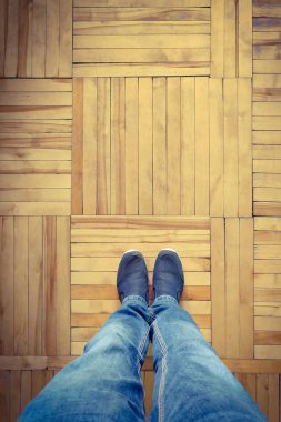 Kırpılmış erkek bacakları tahta parke zeminde spor ayakkabıların içinde duruyor.