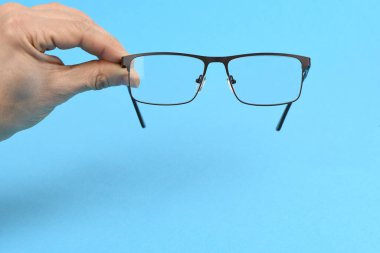 El ele tutuşan siyah gözlükler, mavi arka planda izole. Yüksek çözünürlüklü. Tam alan derinliği.