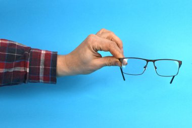 El ele tutuşan siyah gözlükler, mavi arka planda izole. Yüksek çözünürlüklü. Tam alan derinliği.