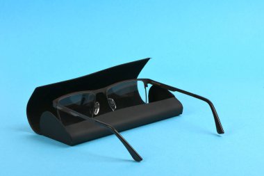 Okuma gözlükleri ve siyah sert çanta mavi arka planda izole. Yüksek çözünürlüklü. Tam alan derinliği.