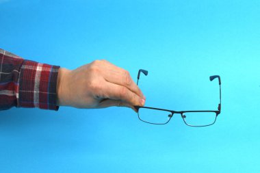 El ele tutuşan siyah gözlükler, mavi arka planda izole. Yüksek çözünürlüklü. Tam alan derinliği.