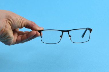 El ele tutuşan siyah gözlükler, mavi arka planda izole. Yüksek çözünürlüklü. Tam alan derinliği.